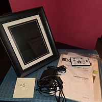 Front view of black HP digital picture frame with accessories laid beside it