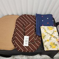 All four sets stacked: tan, brown striped with napkins, blue floral, cream floral