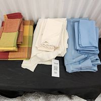 Three stacks of tablecloths and napkins: red multicolour, cream, blue