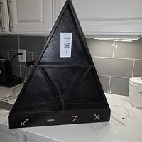 Front view of black wooden triangular shelf, two shelves, gold zodiac symbols on base