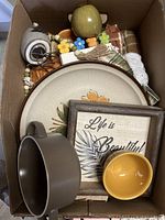 Box showing dinner plate, bowls, framed sign, bead garland, tablecloth and other decor