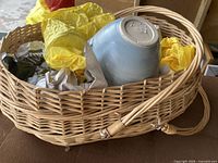 Wicker basket containing wrapped glassware and blue pottery bowl