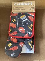 Packaged Cuisinart 4-piece BBQ textile set showing apron, towel, oven mitt, pot holder and branding