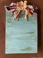 Front of turquoise wooden board with burlap flower and ribbons
