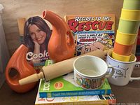 Overall shot showing cookbooks, oil dispensers, rolling pin, bowl, mug, tumblers