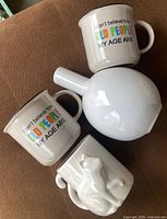 Two quote mugs, cat mug, and white globe vase on couch