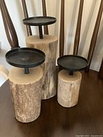 Three wood log base candle holders with black metal plates on round wooden table