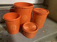 Front view of four orange canisters, two with lids