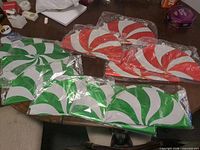 Multiple sealed packs of red and green peppermint swirl foil balloons on table