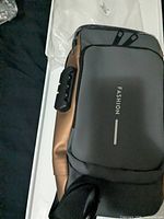 Top view of gray and bronze anti-theft sling bag showing combination lock and packaging