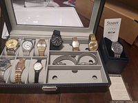 Open display case showing multiple watches, loose bracelets and Stauer watch in holder