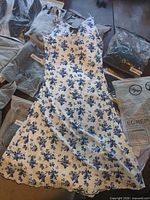 Blue floral midi dress laid flat, surrounding sealed packages visible