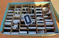 Open box with partitioned tray showing stacks of metal letter plates