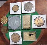 Overview of two gold-clad bars and six tokens/medals on green felt