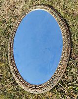 Full view of oval mirror front showing reflective surface and ornate gold frame