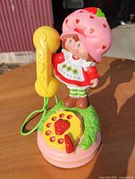 Front view showing Strawberry Shortcake figure, yellow handset, pink base, strawberry-shaped rotary dial