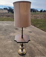 Full view of brass floor lamp with wood table and shade