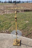 Full view of brass floor lamp with harp and glass tray shelf
