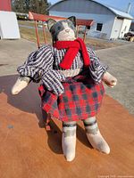 Cat doll seated on wooden rocking chair showing overall appearance and clothing