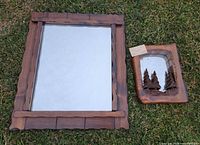 Large rectangular wood framed mirror and smaller carved wood mirror side by side on grass