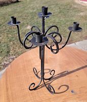 Side view of wrought iron candelabra on table showing four candle cups and scrolled design