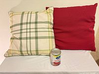 Green plaid pillow beside red pillow with can for scale