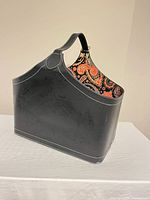 Full view of black faux leather storage bin, showing strap and paisley lining