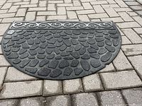 First rubber semi-circular mat on interlocking stone surface showing raised cobblestone texture and scroll border