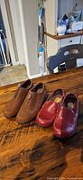 Both pairs of shoes on table (brown and red)