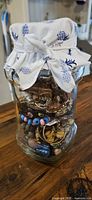 Full view of clear glass jar filled with assorted jewelry, fabric-tied lid visible