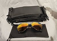 Stack of 24 black drawstring pouches and sunglasses laid in front