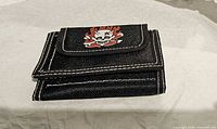 Closed wallet showing front flap with flaming skull graphic and white stitching