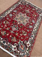 Oblique view of full rug showing red field, ivory border, fringe