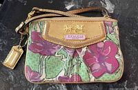 Front view of Coach floral canvas wristlet showing print, leather trim, plaque and hangtag
