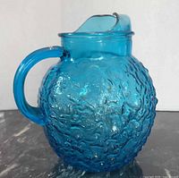 Front view of blue textured glass pitcher showing handle and ice lip