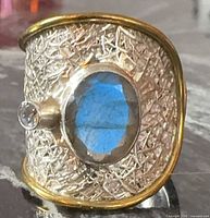 Front view showing labradorite cabochon and clear accent stone on textured wide band with gold trim