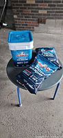 Two sealed bags and lidded plastic bucket of Alaskan ice melter on small table