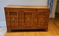 Front view of walnut credenza showing three paneled doors and chrome pulls