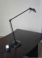 full view of black adjustable arm desk lamp on desk with power cord visible