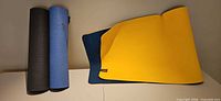 All three mats displayed: black and blue mats rolled, LOLE yellow-navy mat partially unrolled