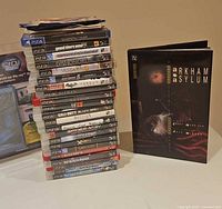 Stack of PS3/PS4 games with Arkham Asylum book beside stack