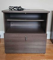 Front view of laminate media and filing cabinet showing open shelf, locking file drawer, and power cord