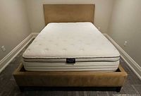 Full view of queen mattress on tan upholstered bed frame with headboard