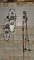 Full view of Yukon snowshoes hung on wall beside two pairs of telescoping poles