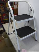 Front view of 2-step folding stool showing white frame and black treads