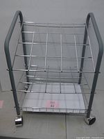 Front view of gray metal rolling cart with three chrome wire shelves and casters