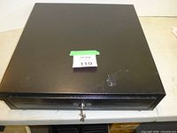 Closed black APG cash drawer with key in lock