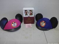 Two Mickey ear hats beside boxed Mickey and Minnie figurines