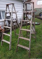 Two wooden A-frame step ladders outdoors on grass