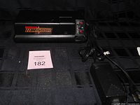 Front view of MotoMaster Eliminator starter showing logo and control panel with attached power cord and AC adapter